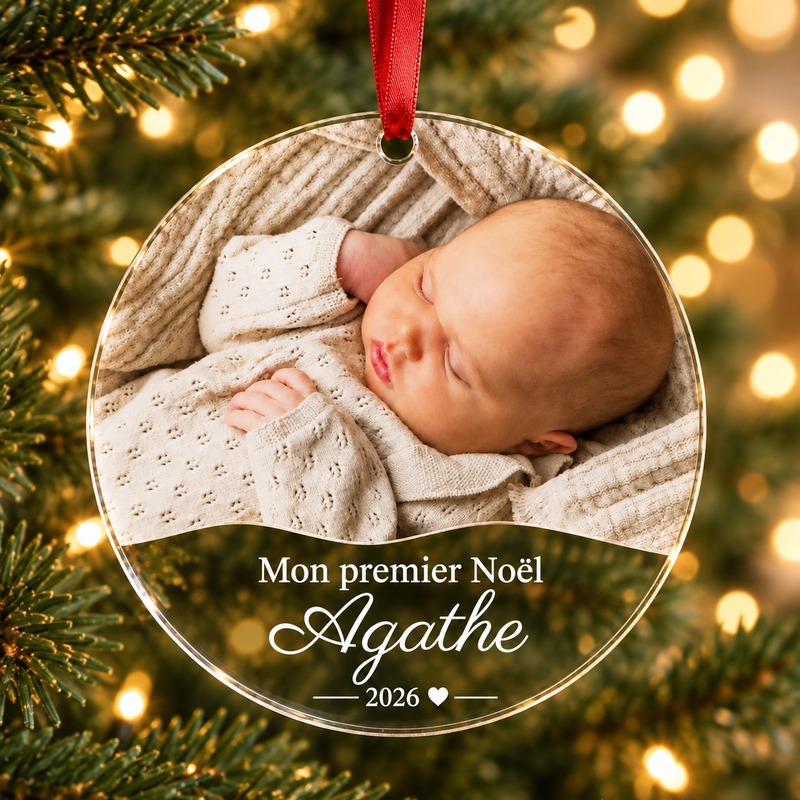 Boule de Noël personnalisée en plexiglas transparent avec photo de bébé, prénom Agathe et inscription « Mon premier Noël 2026 », suspendue dans un sapin.